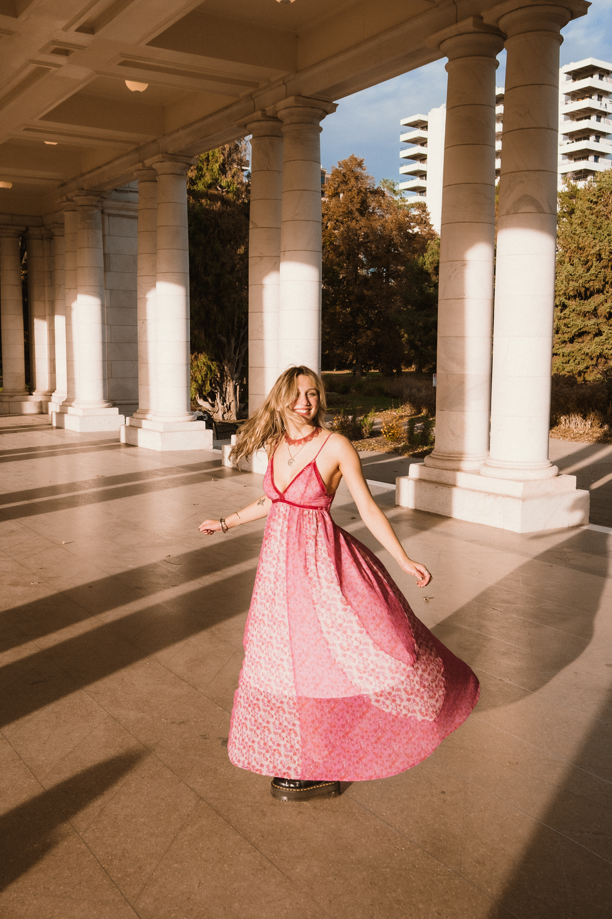 Graduate twirling in a pink dress between tall stone columns
